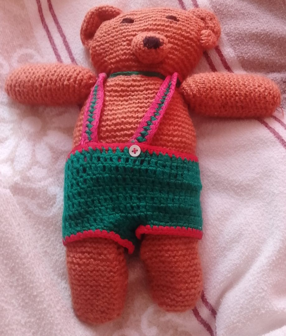 gehäkelter Teddybär, der eine grüne Latzhose trägt